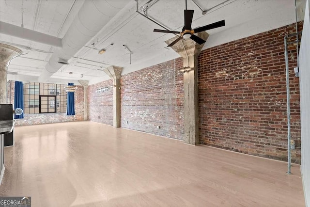 interior space with a ceiling fan, brick wall, and wood finished floors