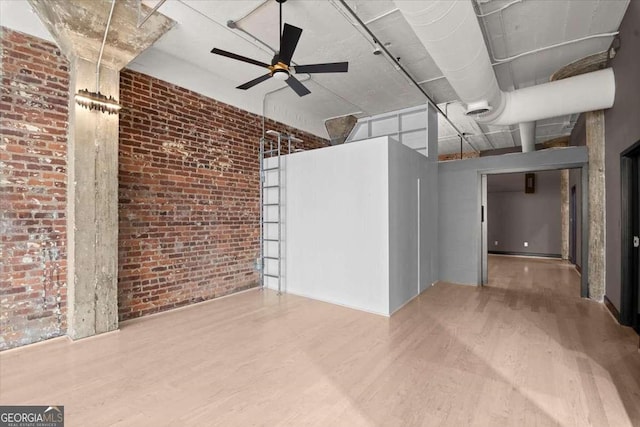 empty room featuring brick wall, ceiling fan, and wood finished floors