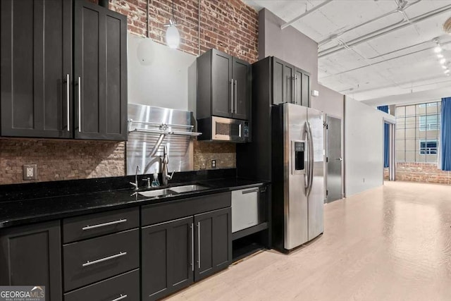 kitchen featuring brick wall, appliances with stainless steel finishes, a sink, and dark cabinets