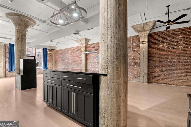 interior space with decorative columns, brick wall, ceiling fan, light wood-style flooring, and dark cabinets