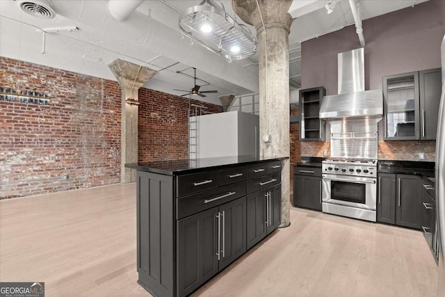 kitchen with wall chimney exhaust hood, dark countertops, high end stove, and glass insert cabinets