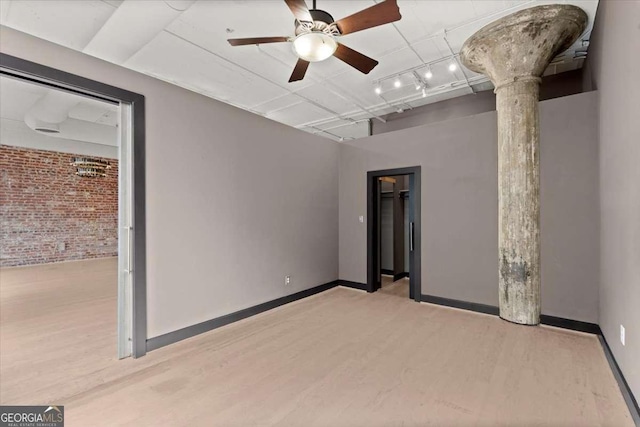 unfurnished room featuring baseboards, brick wall, and light wood-style floors