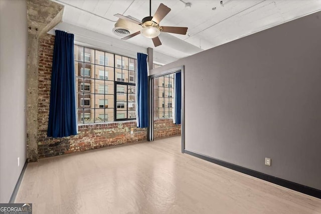 unfurnished room with brick wall, wood finished floors, visible vents, baseboards, and a ceiling fan