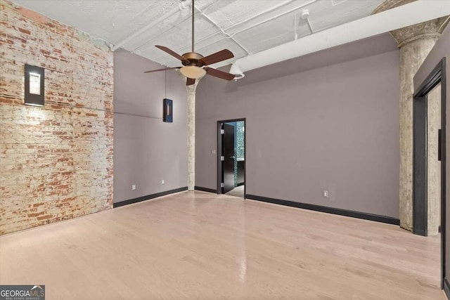 spare room with brick wall, a ceiling fan, a towering ceiling, baseboards, and light wood-type flooring