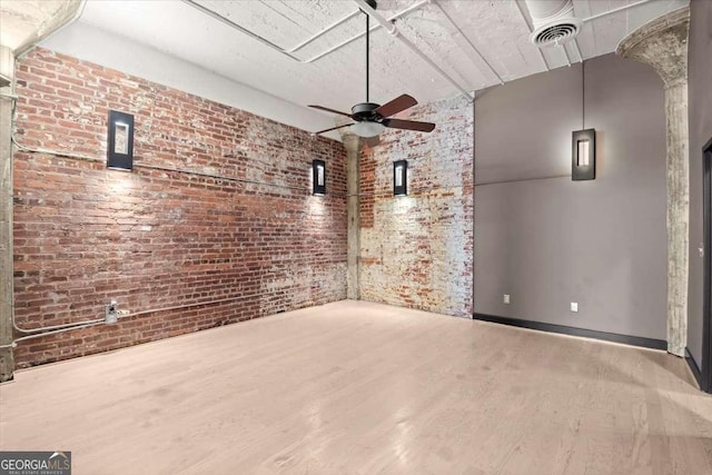 empty room featuring visible vents, a ceiling fan, brick wall, wood finished floors, and baseboards