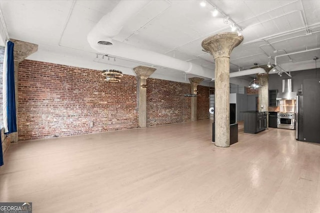 below grade area featuring rail lighting, brick wall, visible vents, and wood finished floors