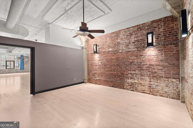 unfurnished living room with ceiling fan, brick wall, and wood finished floors