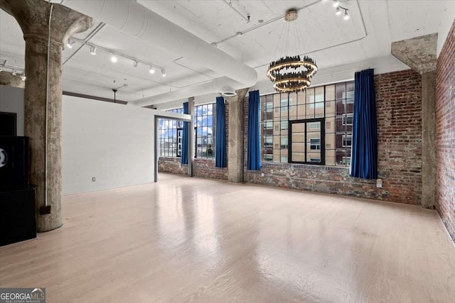 interior space with brick wall, wood finished floors, rail lighting, and an inviting chandelier