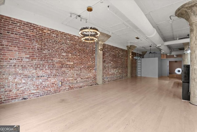 spare room featuring a chandelier, brick wall, and wood finished floors