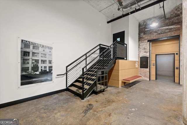 staircase with concrete flooring, elevator, baseboards, and a high ceiling