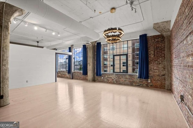 empty room with brick wall, track lighting, a notable chandelier, and wood finished floors