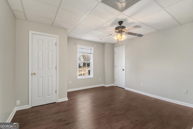 spare room featuring dark wood-style floors, a drop ceiling, ceiling fan, and baseboards