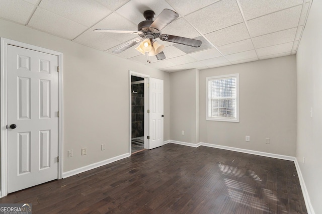 unfurnished bedroom featuring a ceiling fan, baseboards, a drop ceiling, and dark wood-type flooring