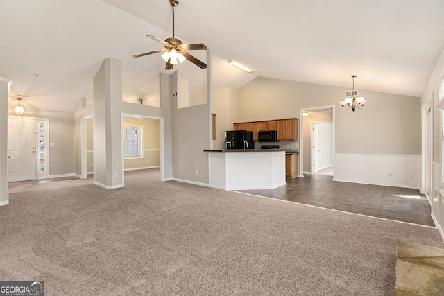 unfurnished living room featuring high vaulted ceiling, dark colored carpet, and ceiling fan with notable chandelier