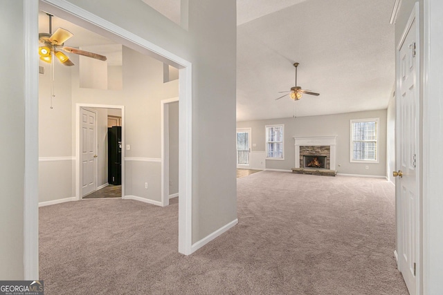 unfurnished living room with light carpet, high vaulted ceiling, a ceiling fan, and a stone fireplace