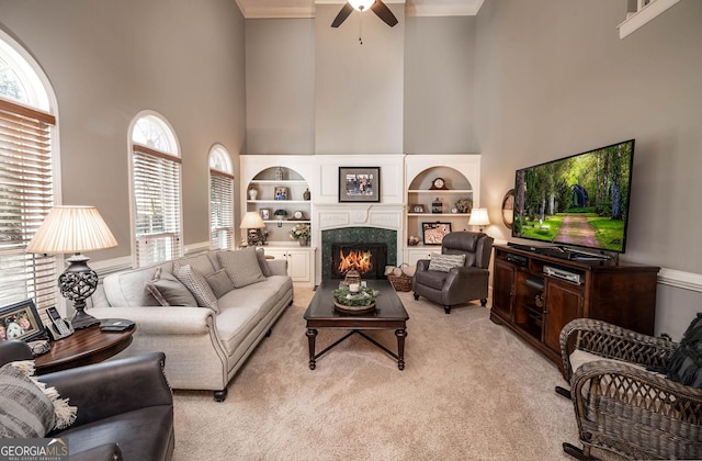 living area with light carpet, a lit fireplace, a high ceiling, and a ceiling fan