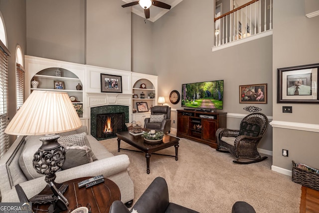 living room featuring baseboards, a ceiling fan, a towering ceiling, carpet flooring, and a fireplace