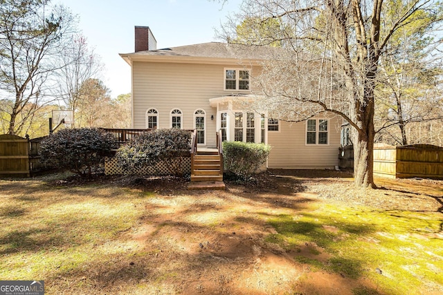 back of property featuring a lawn, a chimney, fence, and a wooden deck