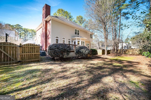 back of house featuring a lawn, a chimney, a gate, fence, and central AC