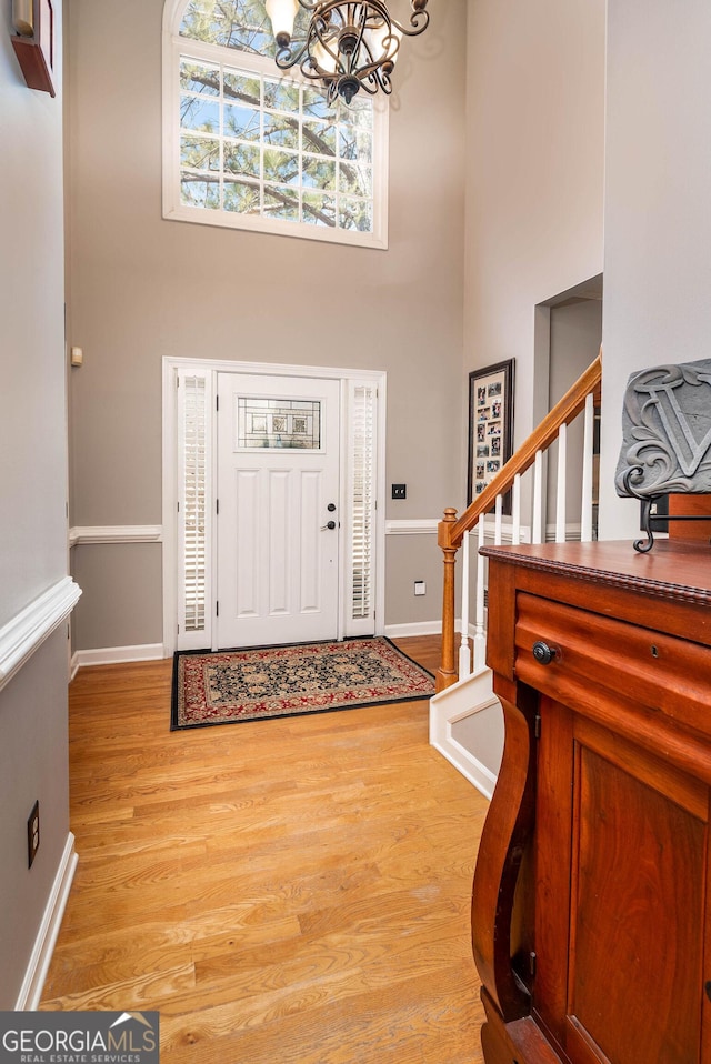 foyer entrance featuring light wood-style flooring, a notable chandelier, a high ceiling, baseboards, and stairs