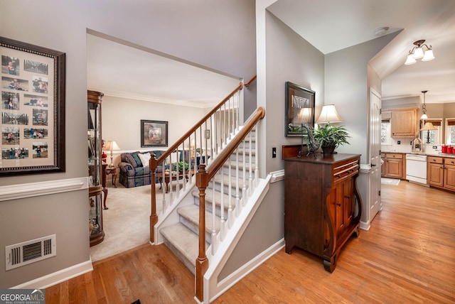 staircase with visible vents, crown molding, baseboards, and wood finished floors