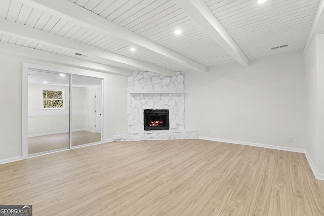 unfurnished living room featuring light wood finished floors, visible vents, baseboards, beamed ceiling, and a fireplace