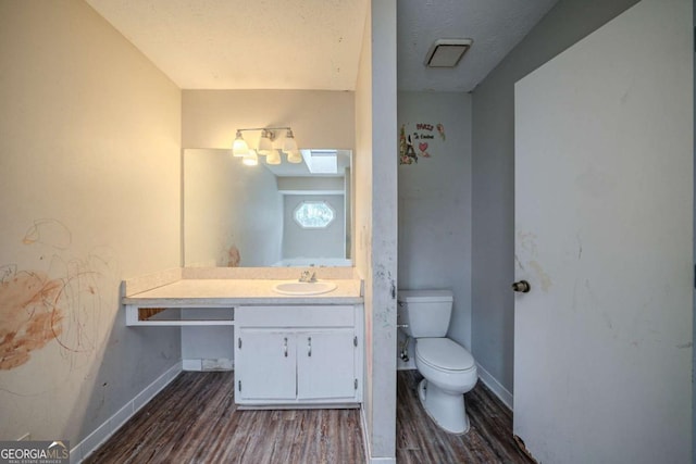 half bathroom featuring a textured ceiling, toilet, wood finished floors, vanity, and baseboards