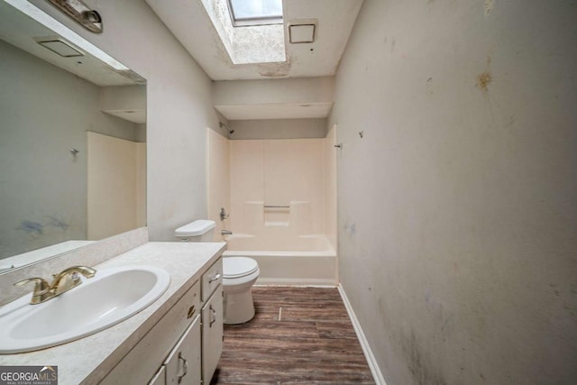 bathroom with a skylight, toilet, vanity, wood finished floors, and baseboards