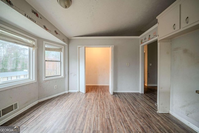 unfurnished bedroom featuring lofted ceiling, baseboards, visible vents, and wood finished floors