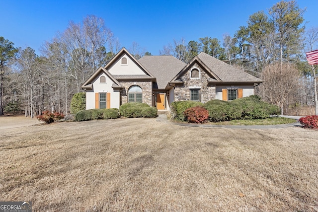 view of front of home featuring stone siding, roof with shingles, and a front yard