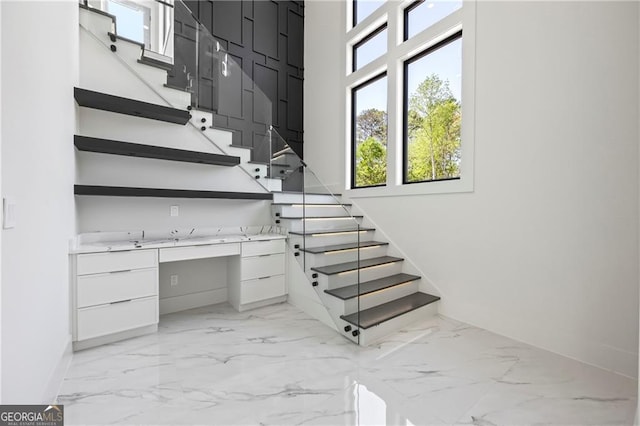 stairway with marble finish flooring, baseboards, plenty of natural light, and a towering ceiling