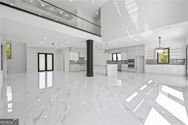 unfurnished living room with a towering ceiling, ornate columns, recessed lighting, and light marble finish floors
