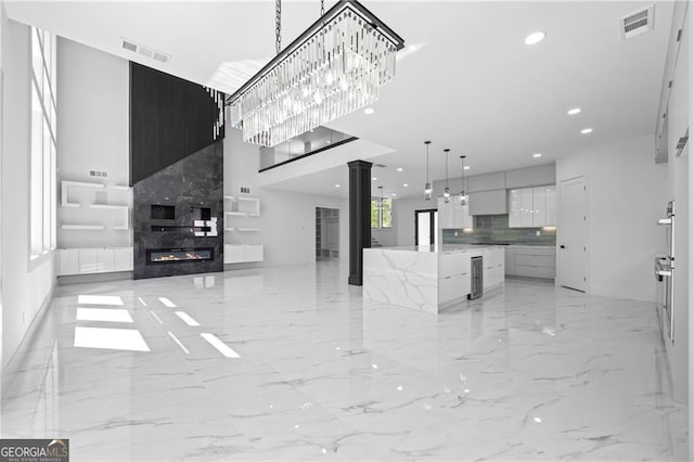 unfurnished living room featuring ornate columns, a towering ceiling, light marble finish floors, a fireplace, and recessed lighting