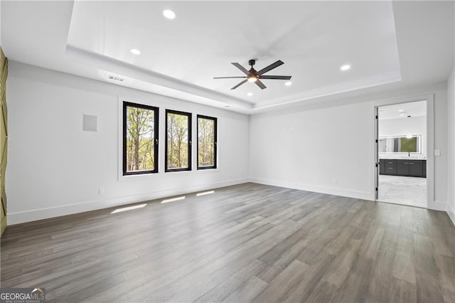 unfurnished living room with a raised ceiling, ceiling fan, wood finished floors, recessed lighting, and baseboards