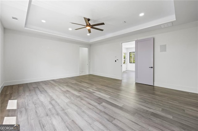 spare room with a tray ceiling, a ceiling fan, wood finished floors, recessed lighting, and baseboards