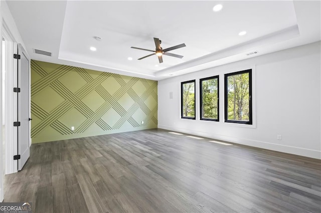 spare room with a raised ceiling, a ceiling fan, recessed lighting, baseboards, and wood finished floors