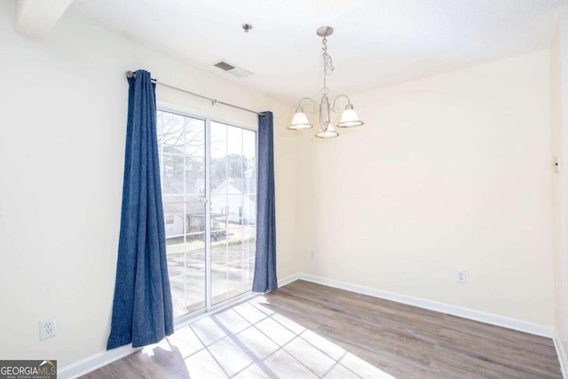 empty room featuring visible vents, a notable chandelier, light wood-style flooring, and baseboards