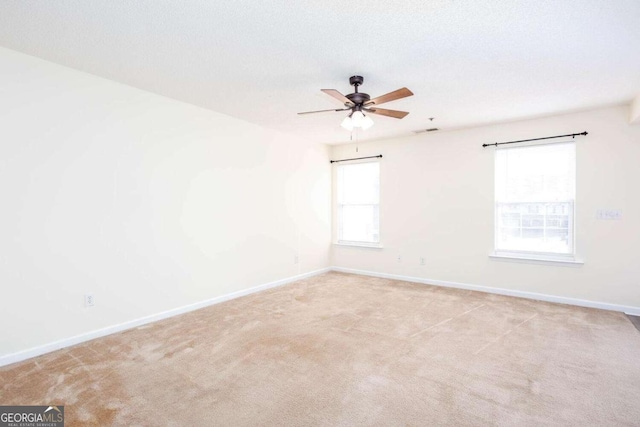 empty room featuring light carpet, ceiling fan, visible vents, and baseboards