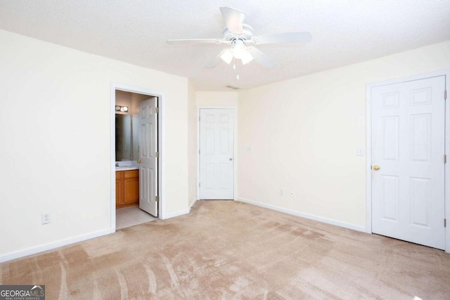 unfurnished bedroom with baseboards, a ceiling fan, light colored carpet, ensuite bath, and a textured ceiling