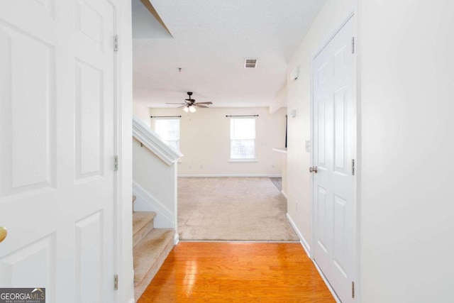 hall featuring visible vents, light wood-style floors, a textured ceiling, baseboards, and stairs