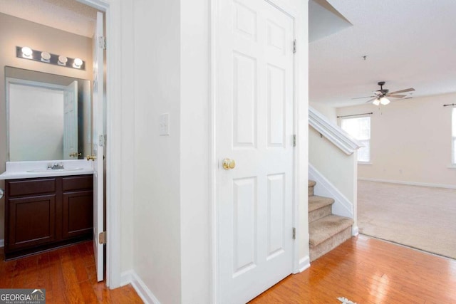 hall with baseboards, a sink, light wood finished floors, and stairs