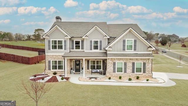 craftsman-style house with board and batten siding, brick siding, a front lawn, and fence