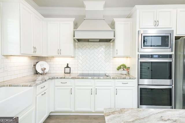 kitchen featuring custom exhaust hood, stainless steel appliances, tasteful backsplash, ornamental molding, and white cabinetry