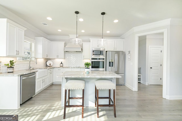 kitchen with appliances with stainless steel finishes, white cabinets, a kitchen island, and decorative light fixtures