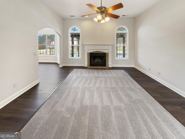 unfurnished living room with a fireplace with flush hearth, a wealth of natural light, dark wood finished floors, and baseboards