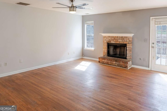 1004 Hamilton Dr, Locust Grove, GA 30248 - unfurnished living room with wood finished floors, visible vents, baseboards, a ceiling fan, and a brick fireplace