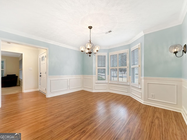 unfurnished dining area with crown molding, a notable chandelier, visible vents, a textured ceiling, and wood finished floors