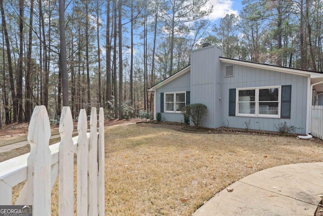 view of side of home with a lawn, a chimney, and fence