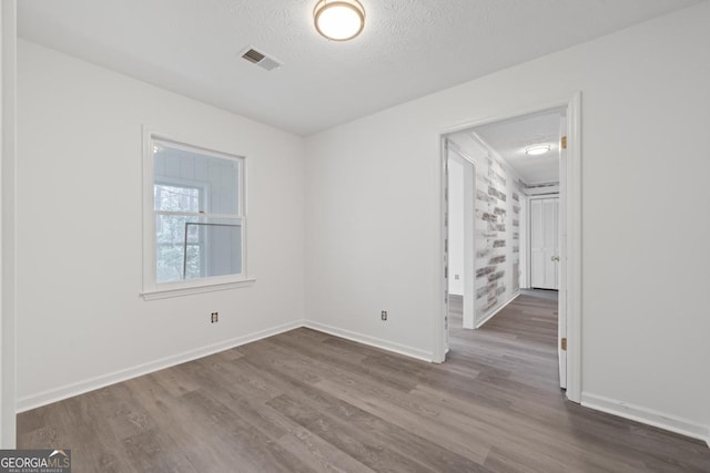 empty room with a textured ceiling, dark wood finished floors, visible vents, and baseboards