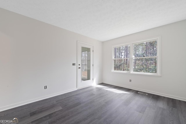 empty room featuring dark wood-style floors, a textured ceiling, visible vents, and baseboards